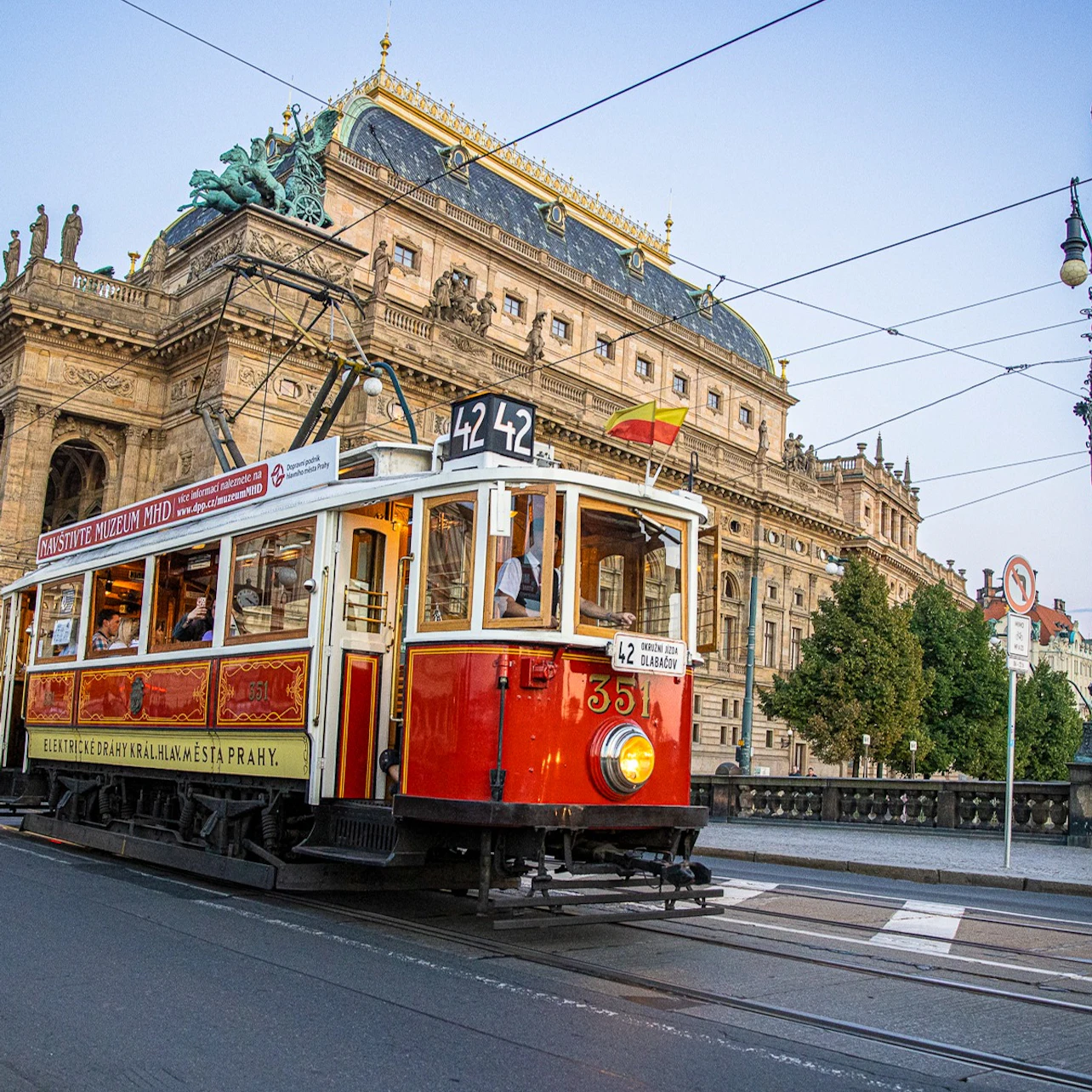 A red and white tram marked "42" passes by a historic building with ornate architecture and a statue on the roof.