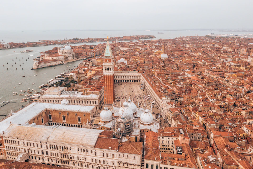 Aerial view of Venice showing St. Mark's Square, the Campanile, and surrounding historic buildings with canals in the background.