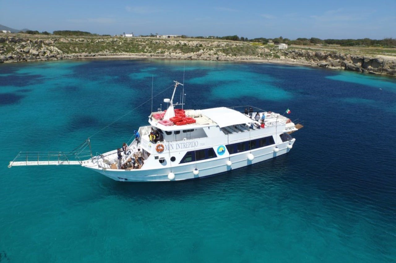 A white boat named "MV INTREPID" is anchored in clear turquoise water near a rocky coastline.