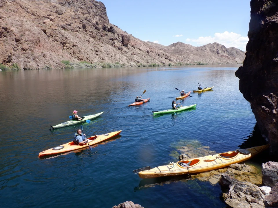 People kayaking on a calm river surrounded by rocky hills under a clear blue sky.