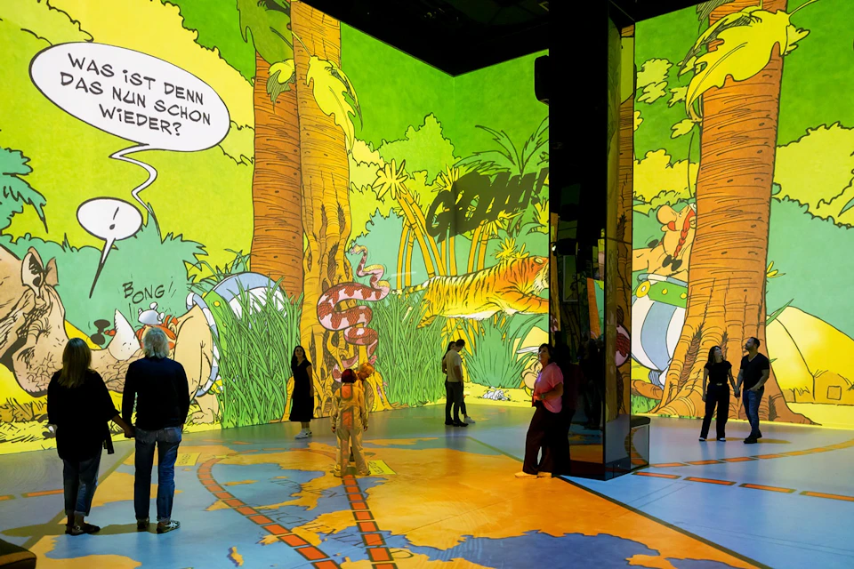 People stand in a brightly lit room with large cartoon jungle-themed designs projected on walls and floors.