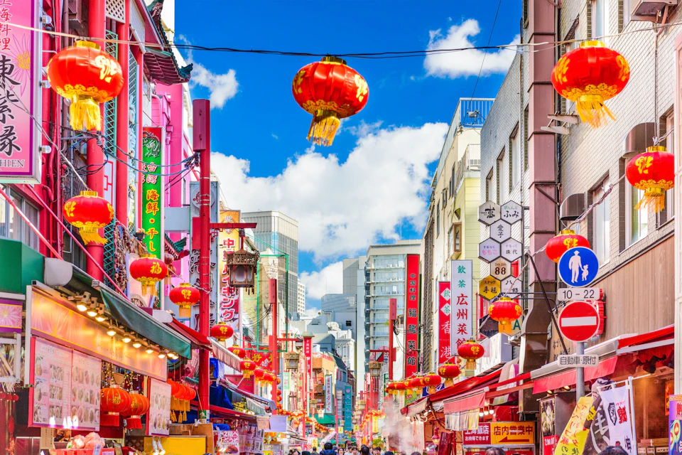 A lively street scene with colorful signs and red lanterns decorating the area under a bright blue sky with clouds.