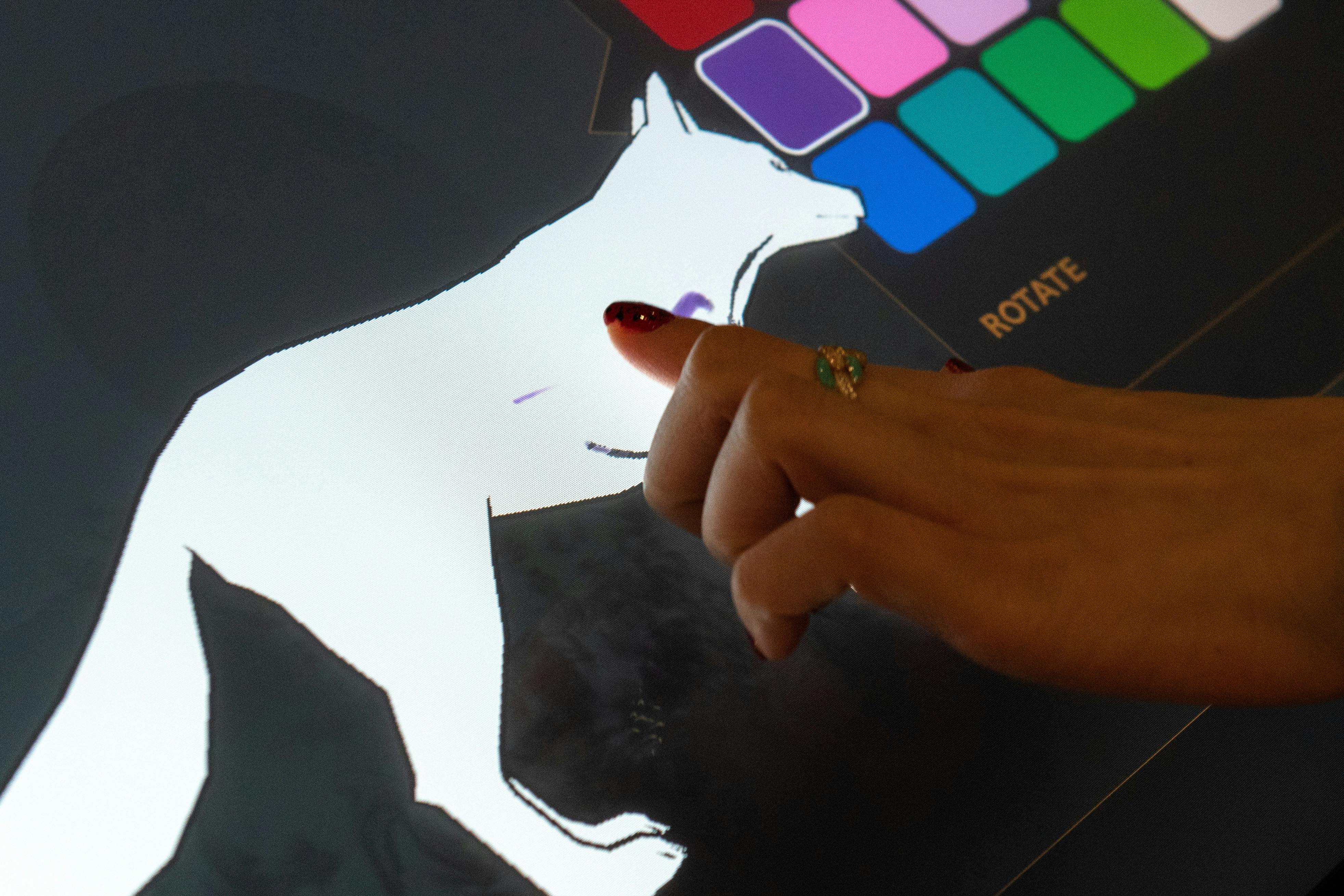 Ruka používá dotykovou obrazovku zobrazující siluetu psa s rámečky pro výběr barev v pravém horním rohu.