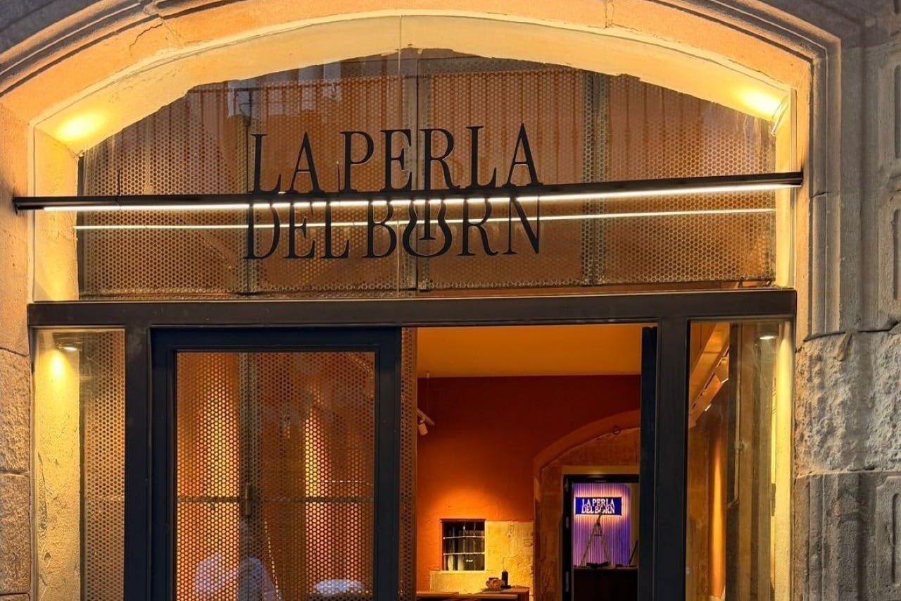 入口处的店面标有“La Perla Del Born” ，玻璃门和温暖的室内装饰。