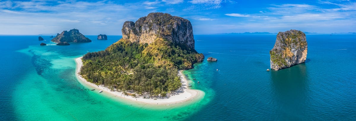 鸟瞰热带岛屿，岛上有郁郁葱葱的绿色植物、白色沙滩，四周环绕着绿松石色的海水和零星的岩层。