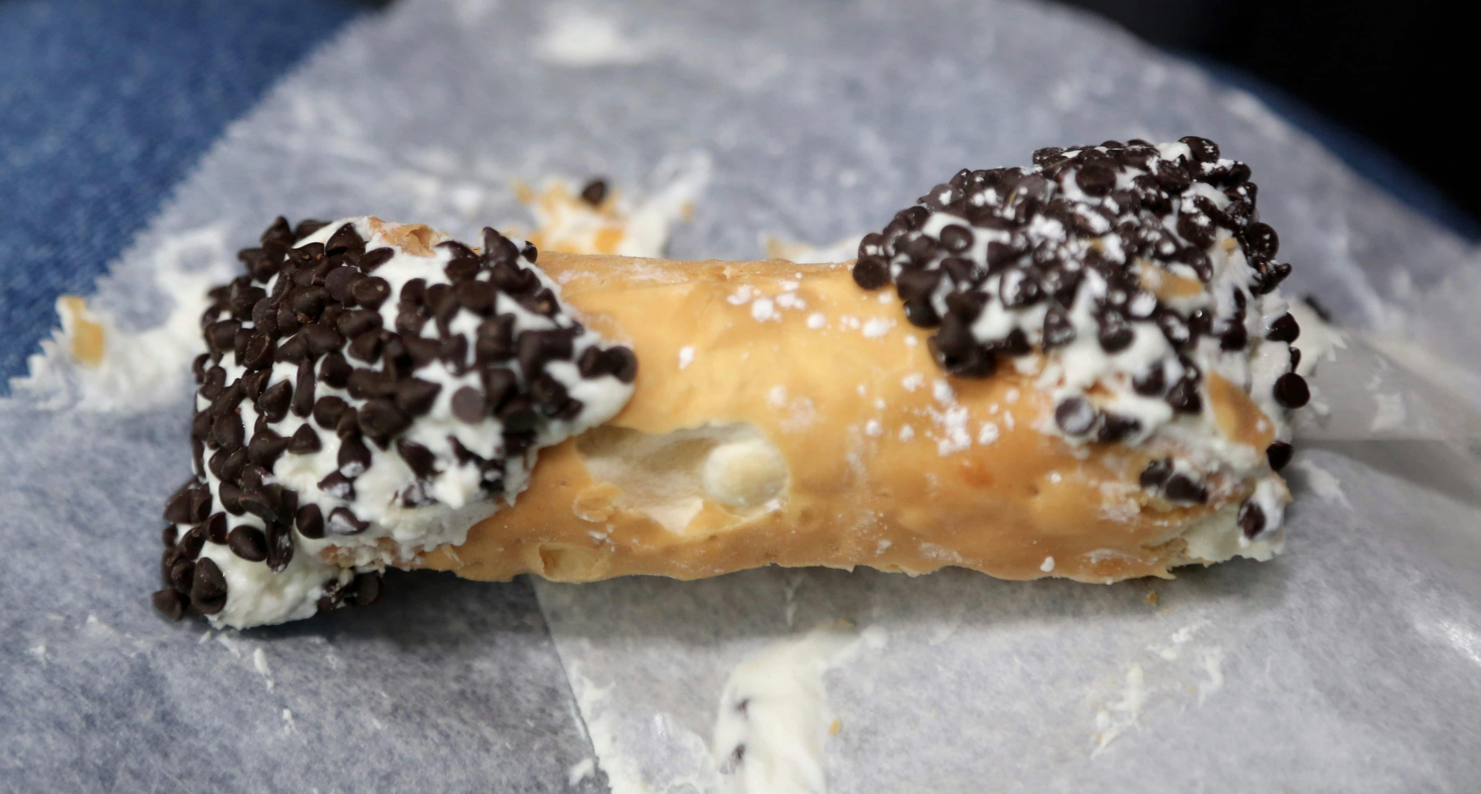 Close-up of a cannoli topped with chocolate chips and powdered sugar, resting on parchment paper.
