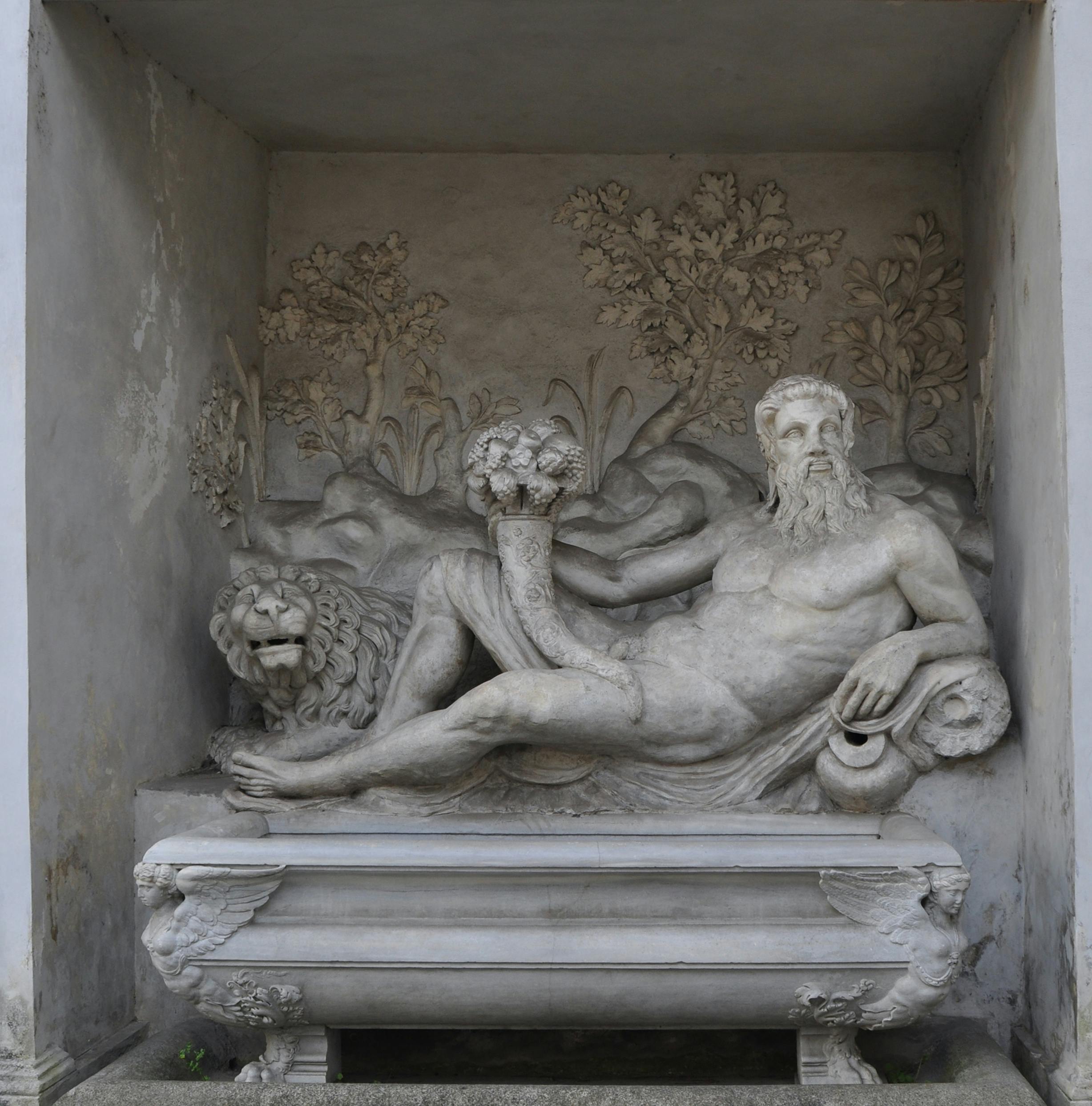 Een stenen reliëf met een liggende man met baard die een cornucopia vasthoudt, met een leeuw naast hem en gebladerte op de achtergrond.