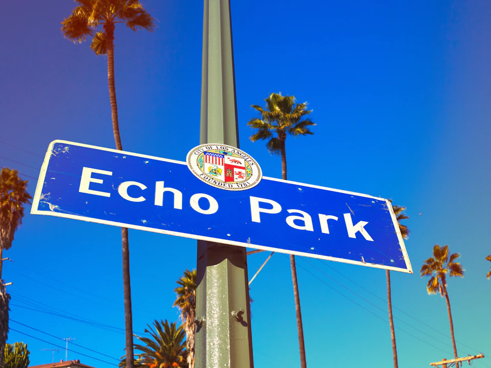 Street sign that reads "Echo Park" mounted on a pole, with palm trees and a clear blue sky in the background.