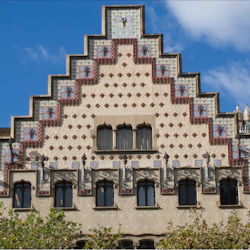 En detaljerad, dekorerad byggnadsfasad med trapptak, geometriska mönster och utsmyckade fönster under en blå himmel med partiella moln.