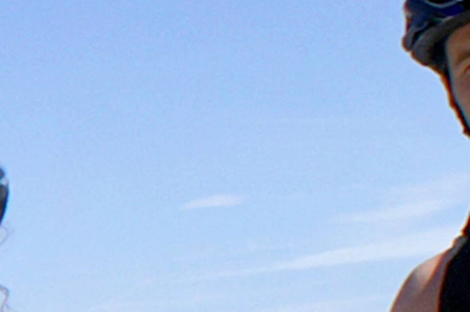 Two people on bicycles, wearing helmets, in front of the Golden Gate Bridge under a clear blue sky.
