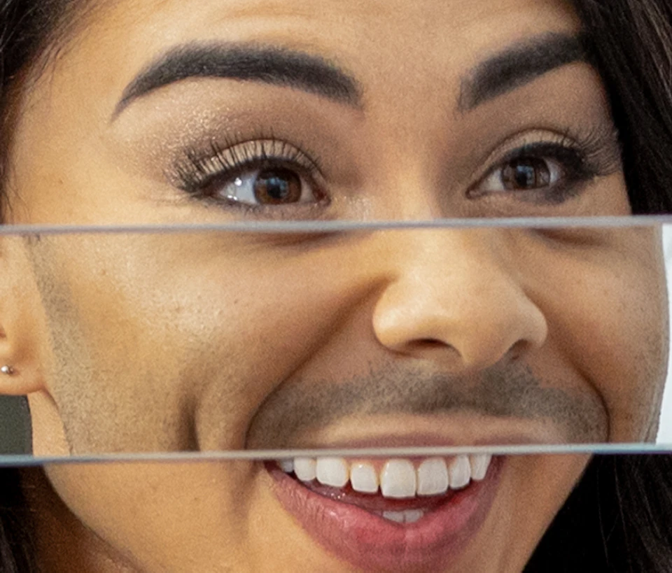 Two people smiling at each other through a striped reflective panel; both are wearing orange shirts.