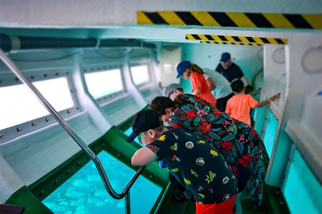 水中の景色を眺めながら、潜水艦のような車両の中の手すりに寄りかかっている人々。