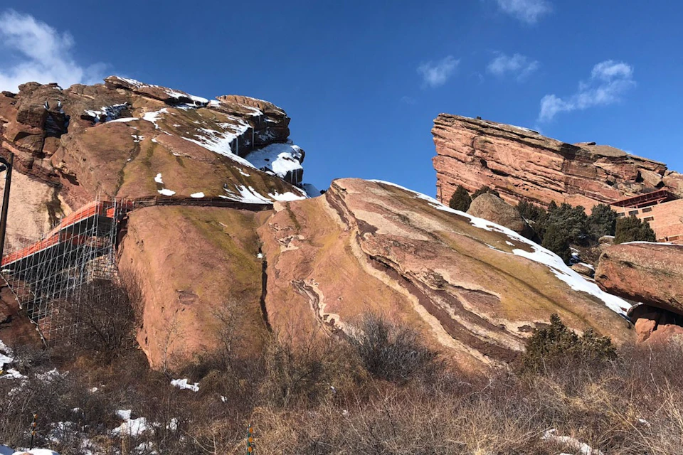 Rugged red rock formations dusted with snow under a clear blue sky; sparse vegetation in the foreground.