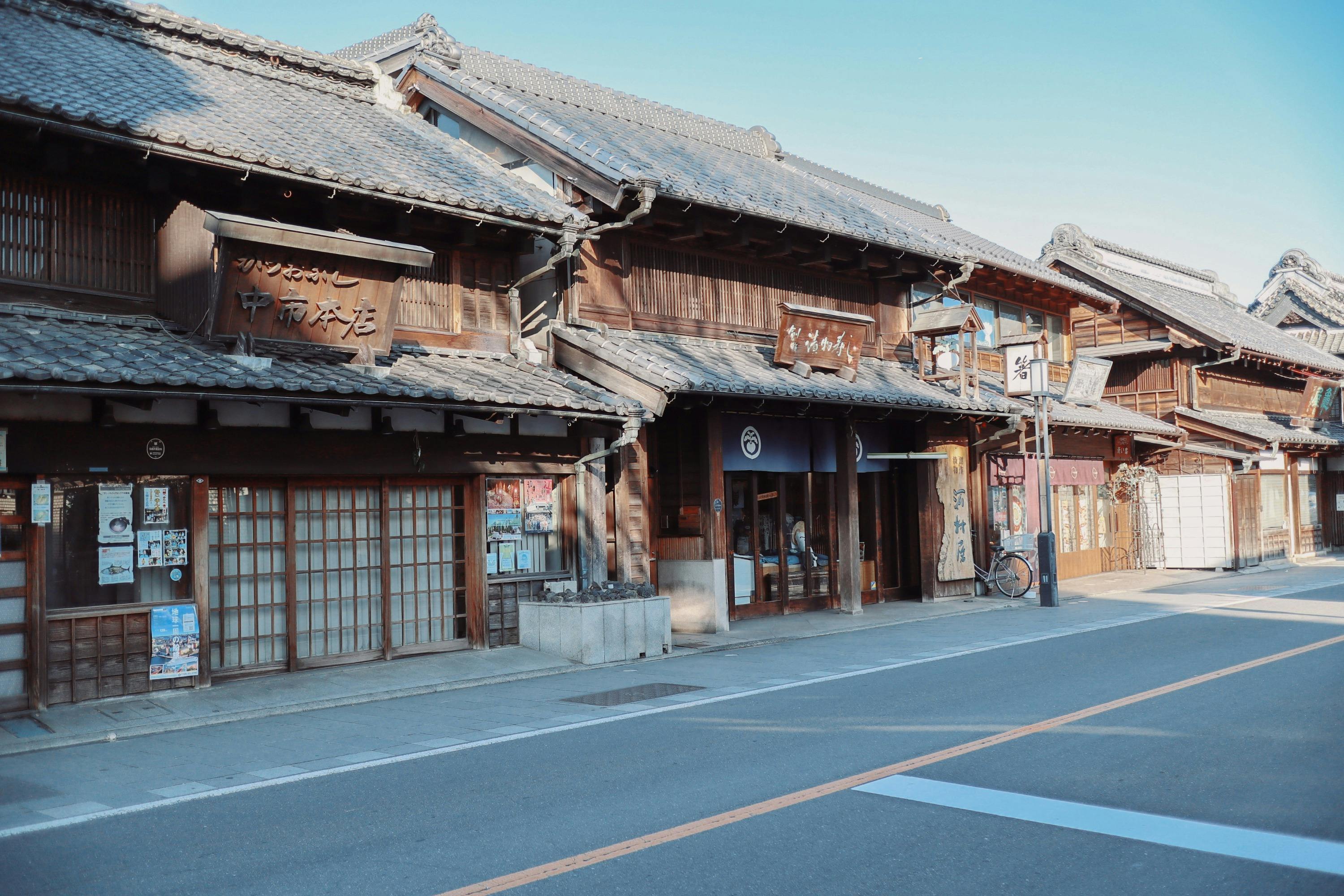 A row of traditional wooden buildings with sliding doors and signage, along a quiet street under a clear blue sky.