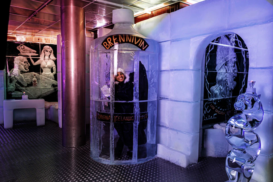 A person inside a large glass bottle labeled "Brennivín," surrounded by icy decor and sculptures in a themed environment.