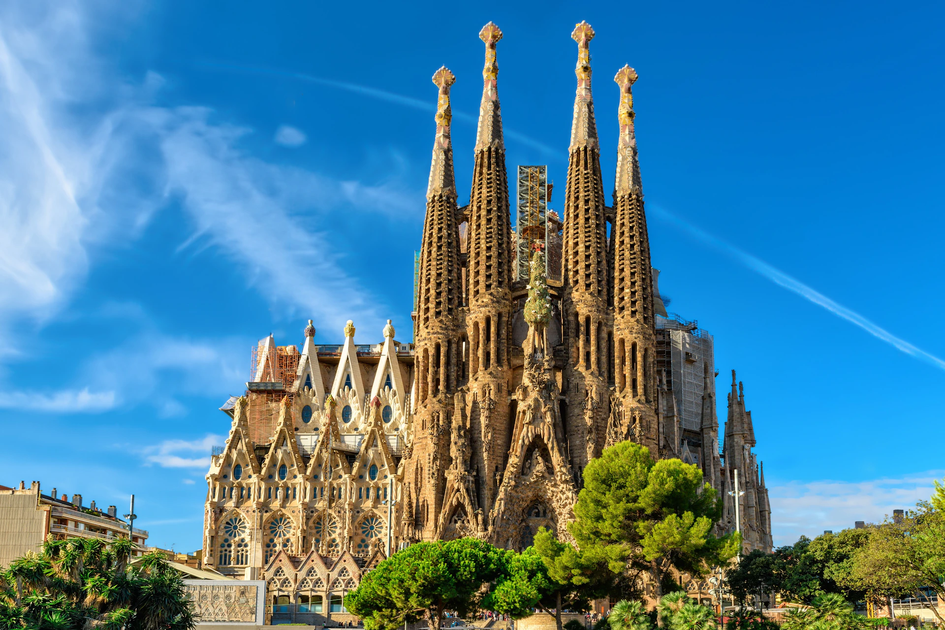 A large, ornate basilica with intricate spires and detailed facades under a blue sky, surrounded by trees.
