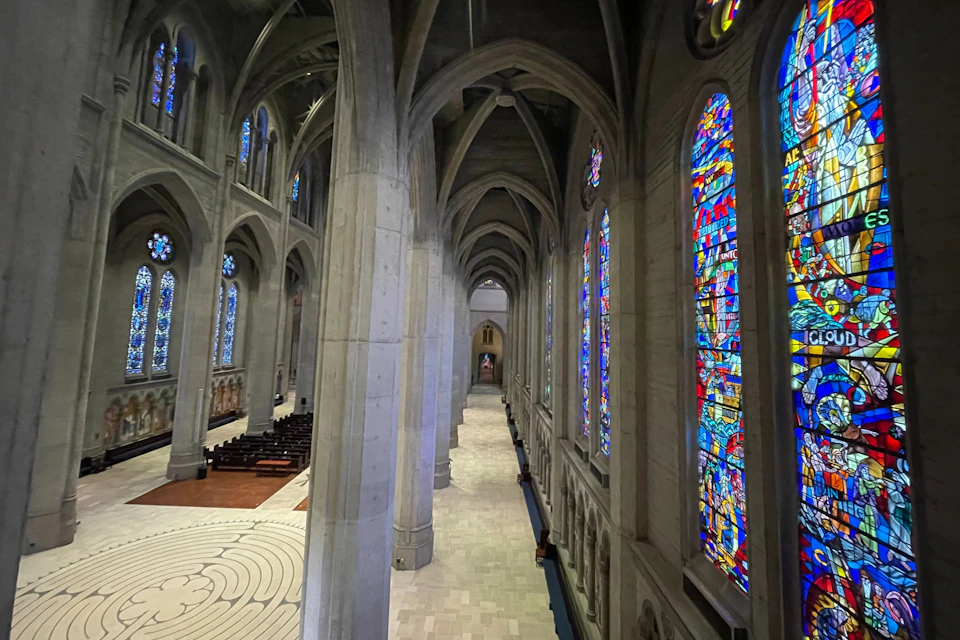 Interior of a gothic-style cathedral with high arches, stained glass windows, and a labyrinth on the floor.
