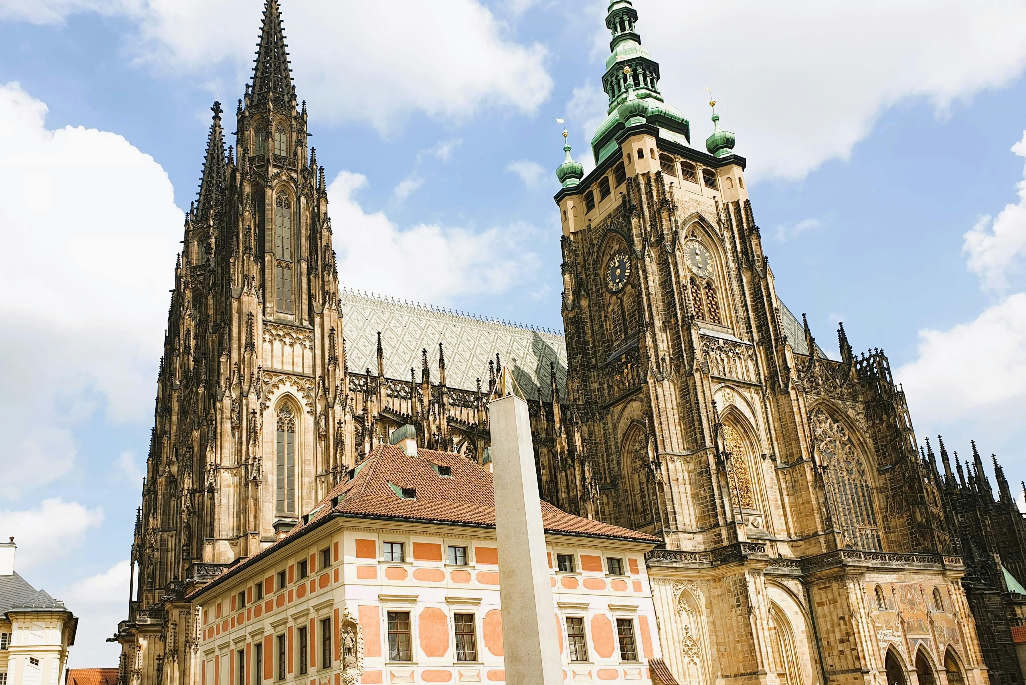 Gothic cathedral with towering spires beside a smaller building with red and white facade, under a partly cloudy sky.