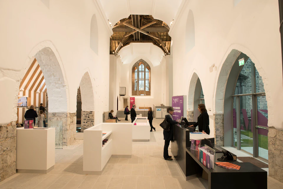 A spacious, white-walled hall with high ceilings, arches, desks, and people interacting and walking.
