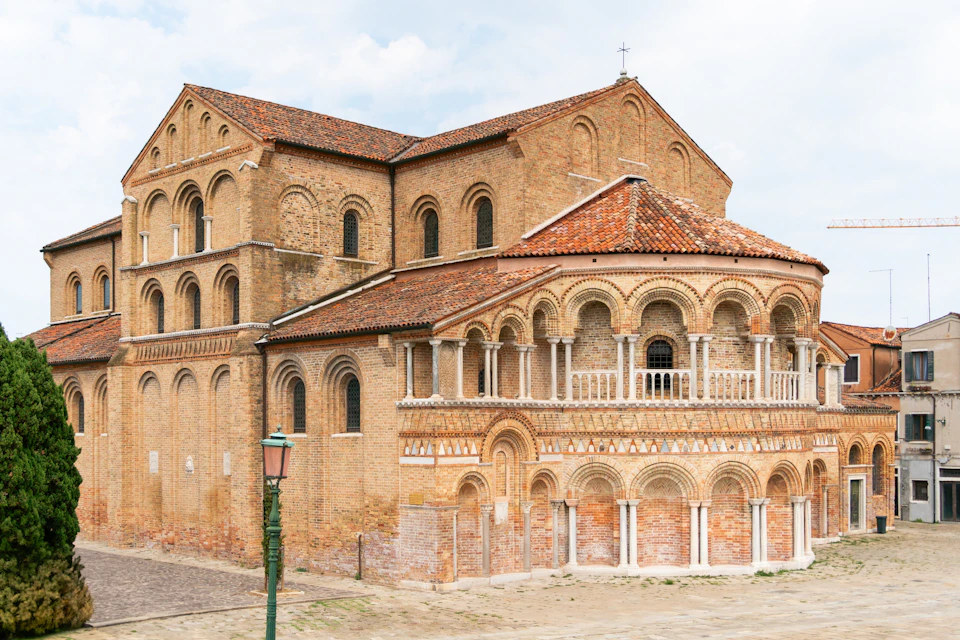 Historic brick church with arched windows and columns, featuring a red-tiled roof, seen on a clear day.