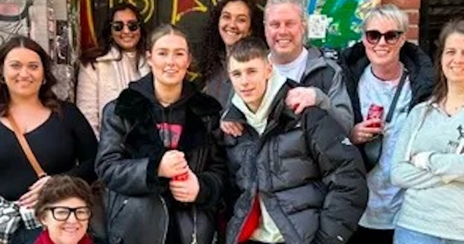 A group of people posing together in front of a graffiti-covered entrance in an urban setting, smiling for the photo.