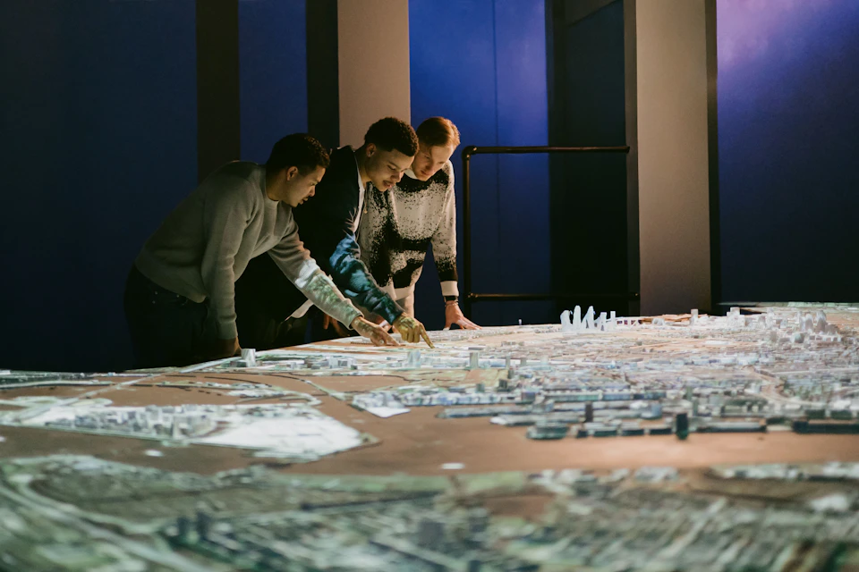 Three people leaning over and examining a large scale model of a city in a dimly lit room.