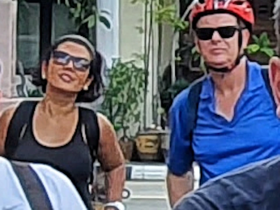 A group of people on bicycles posing under a red archway that reads "Chinatown Singapore" with shops in the background.