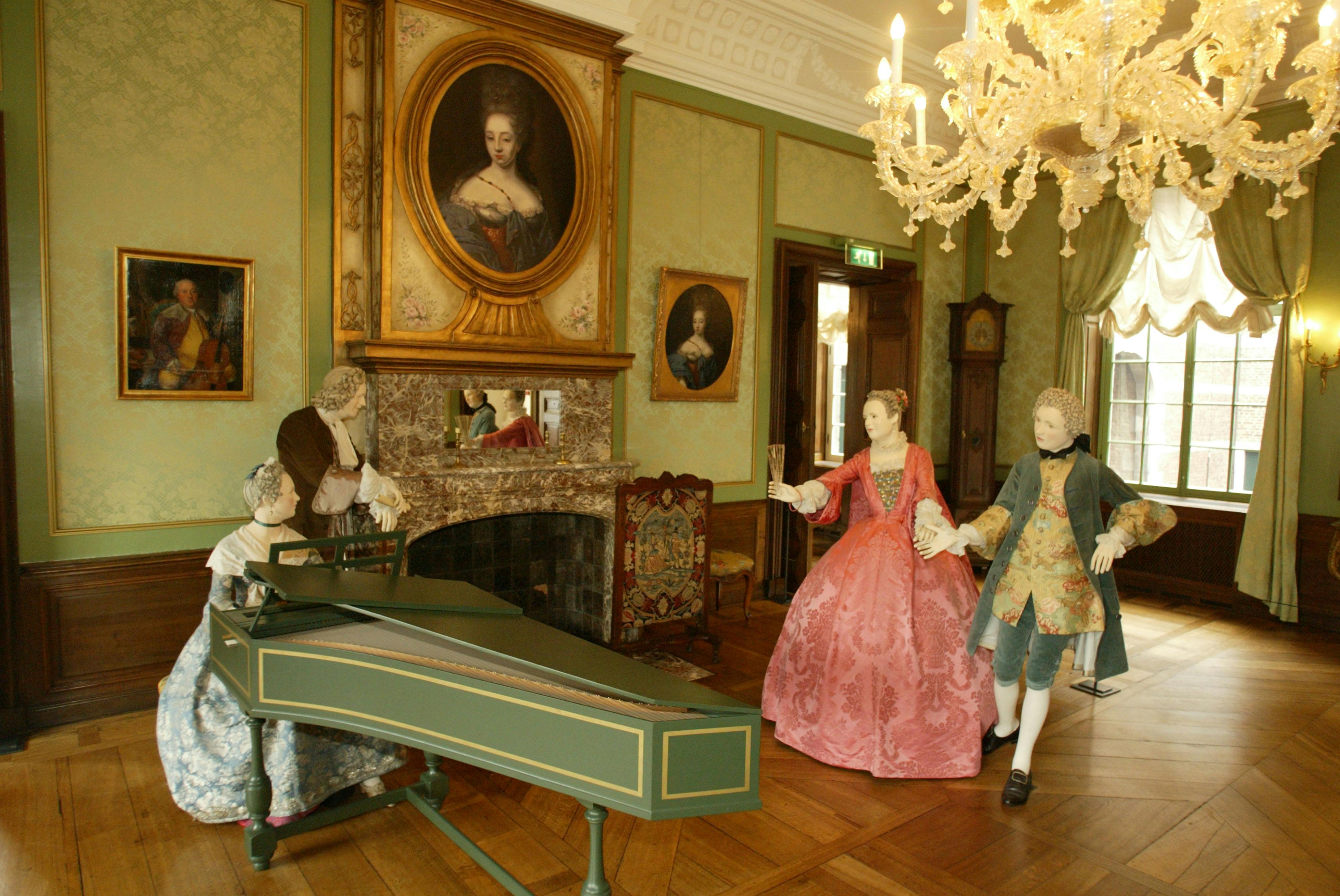 A historic room with a chandelier, harpsichord, paintings, and mannequins dressed in 18th-century attire.
