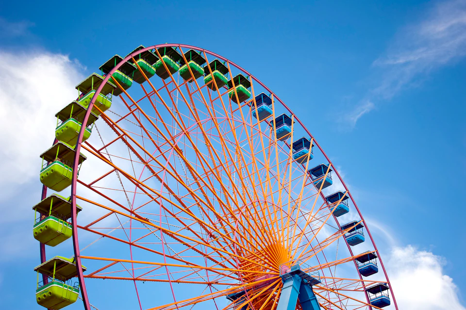 A rollercoaster with an orange track ascending steeply under a clear blue sky, with a platform and supports visible.