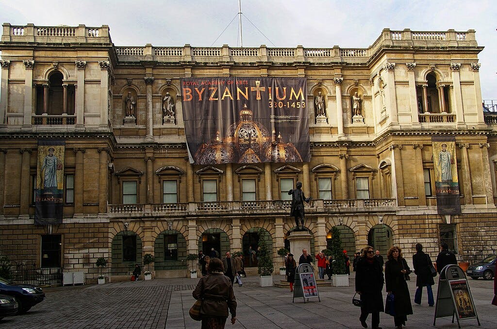 Lidé chodí před historickou budovou s transparenty na výstavu „BYZANTIUM 330-1453“, kterou pořádá Královská akademie umění.