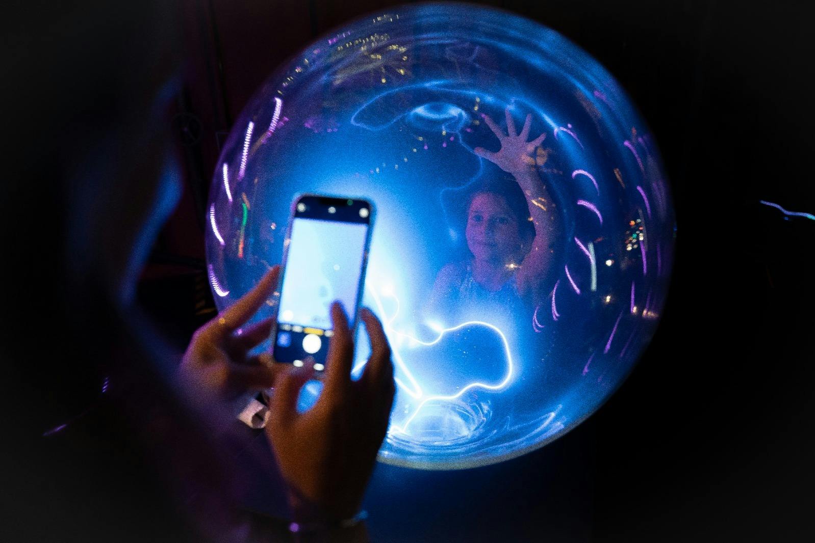 一个人在一个发光的蓝色球体内拍摄一个女人。 她的手紧贴着魔球的表面。