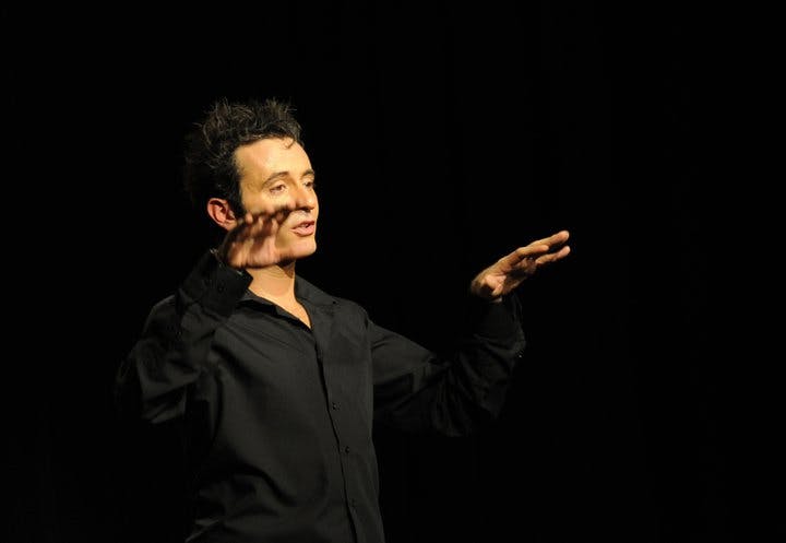 穿着黑色衬衫的黑头发的人，双手在深色背景下做手势。