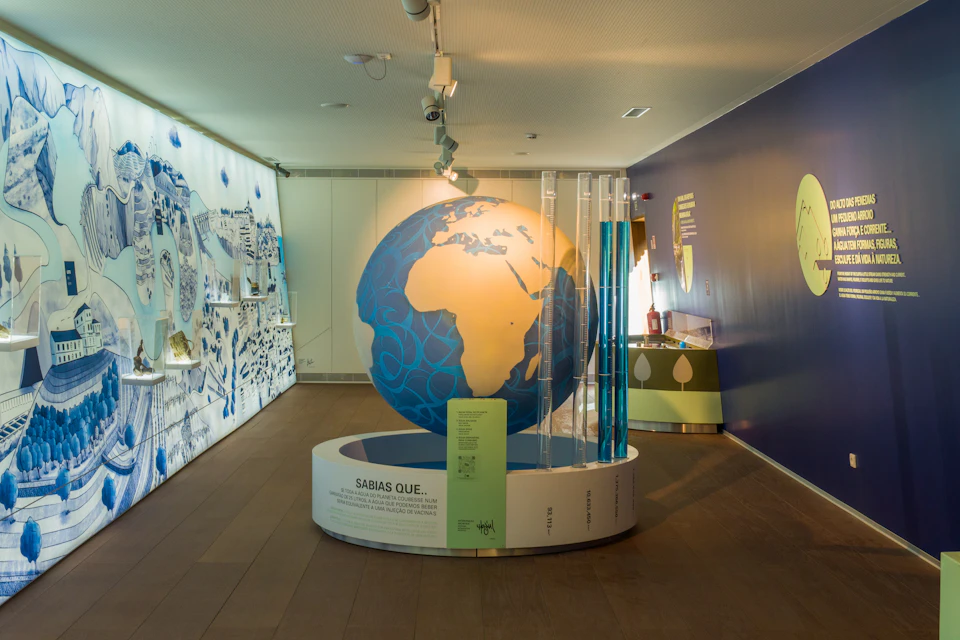 Museum exhibit room featuring a large globe, informational panels, and diagrams on surrounding walls under track lighting.