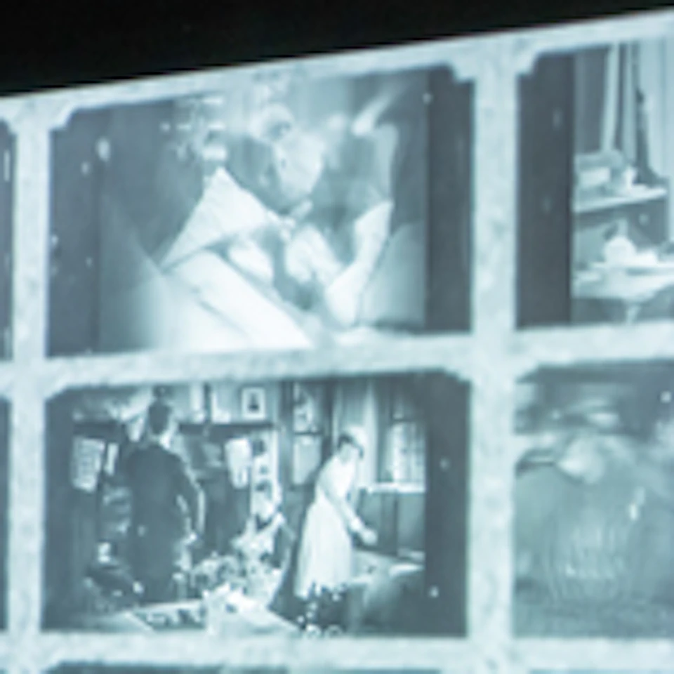 A museum exhibit featuring WWII propaganda posters, a glass display case with artifacts, and a wall of projected black-and-white images.