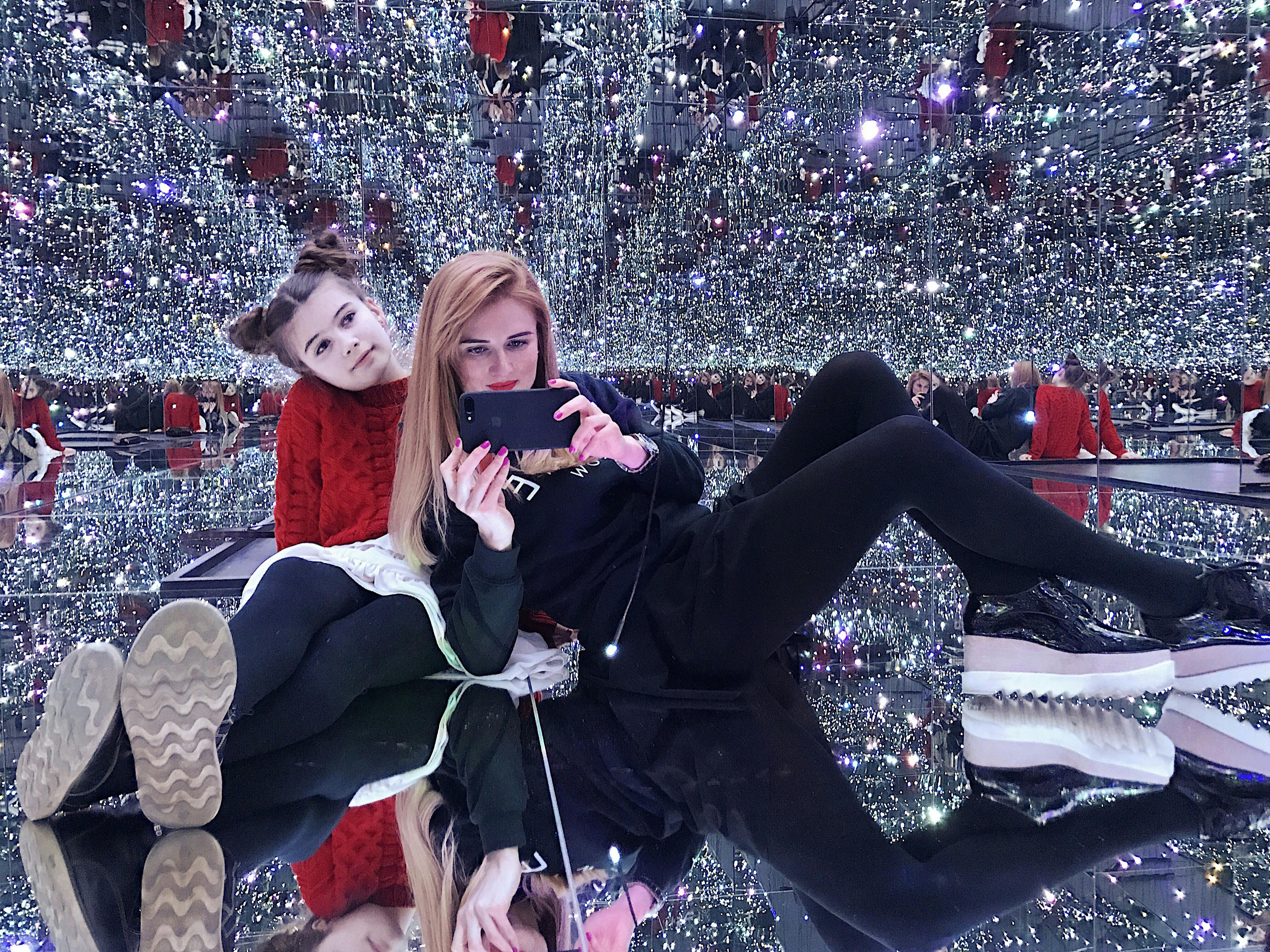 两个人在镜子房间里摆姿势，点缀着许多小灯光，营造出闪闪发光的无限反射效果。