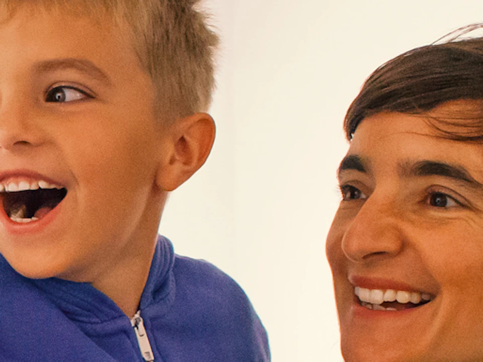 A woman holds a child in her arms in an art gallery. The child is excitedly pointing, and both are smiling.