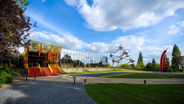 Edificio moderno a specchio adiacente a una scala industriale colorata, con una scultura sferica metallica in lontananza.