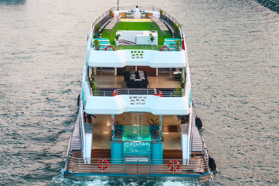 A multi-level yacht with a green rooftop deck, outdoor seating, and a modern design cruising on the water.