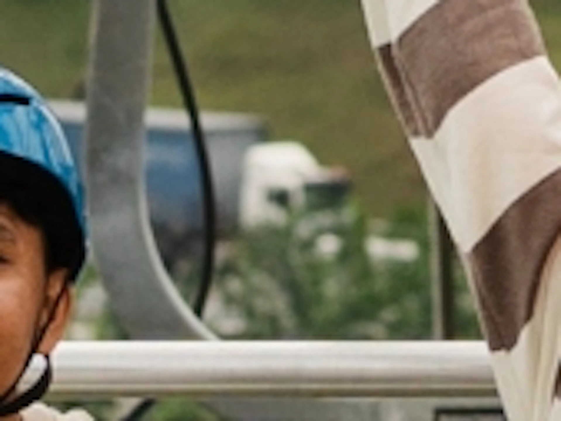 Four people riding a chairlift over a green landscape, smiling and waving with buildings and trees visible below.