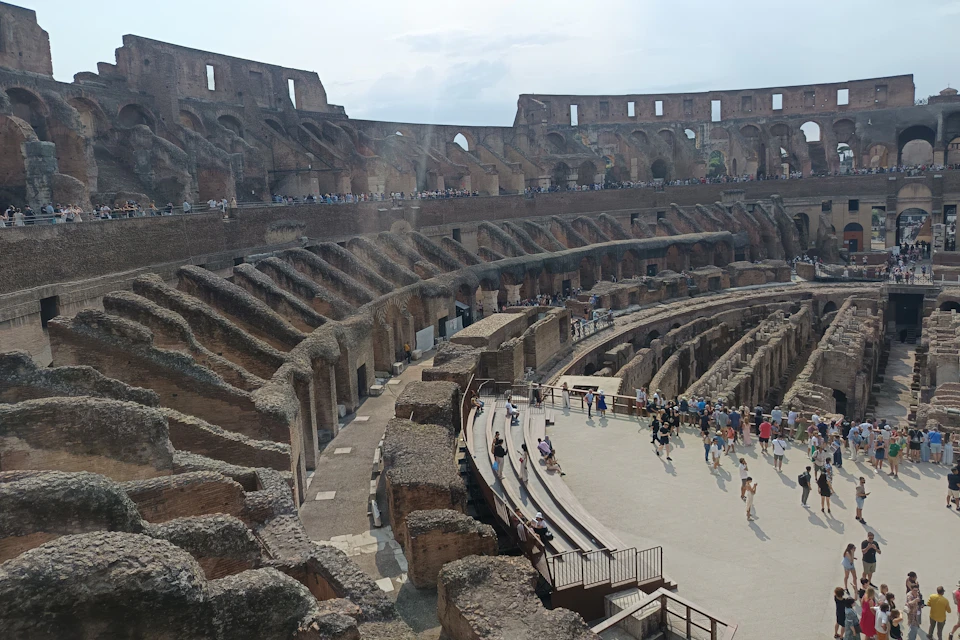 Interior view of the Colosseum in Rome, showing its stone architecture and visitors walking on the arena floor.