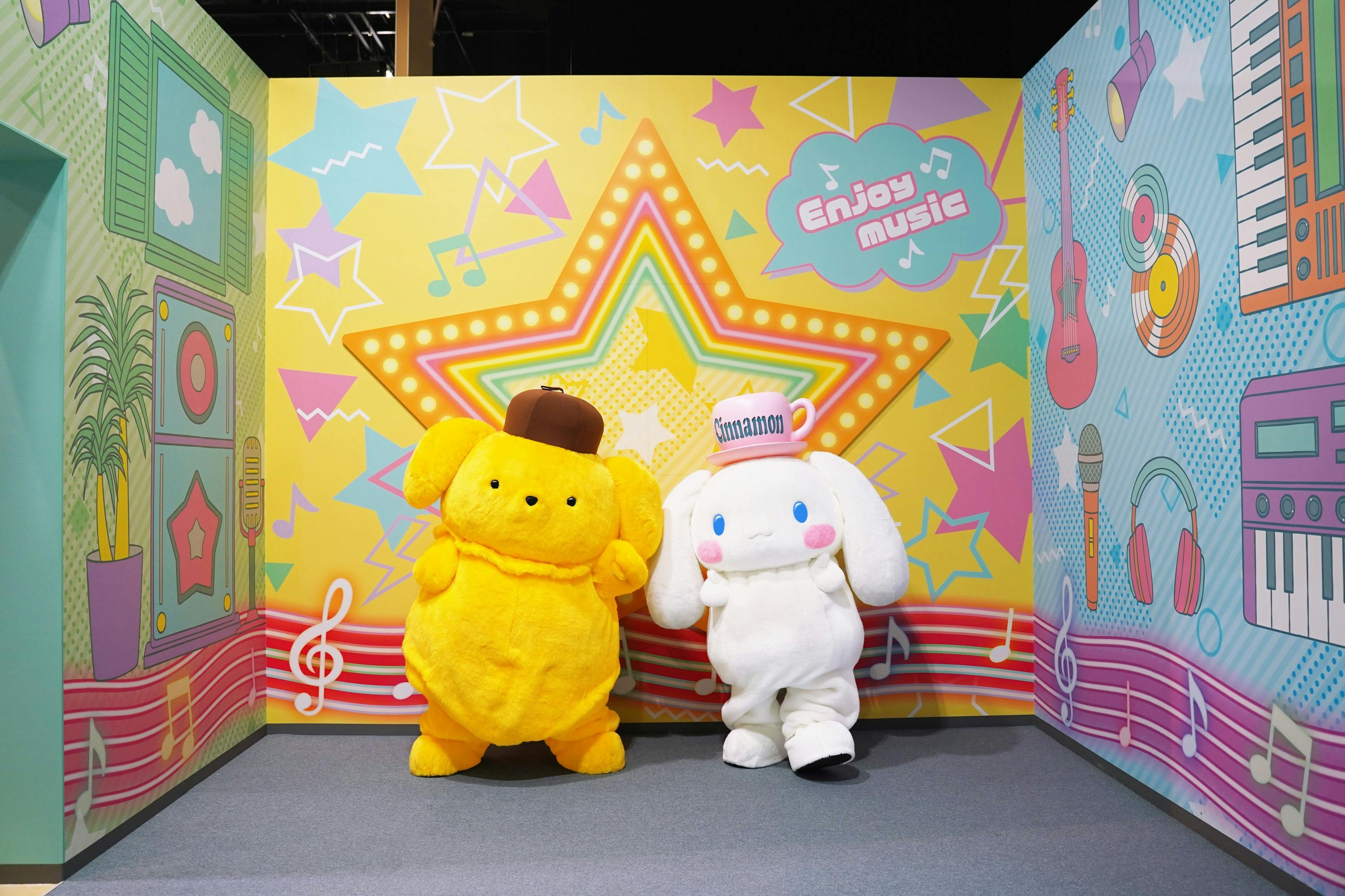 Two costumed characters, a yellow one with a brown hat and a white one with a cap, in front of a colorful backdrop.