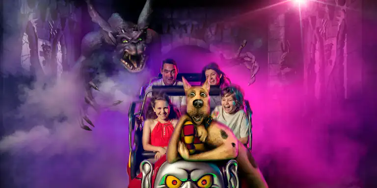 Una família puja a una muntanya russa de temàtica espeluznant amb Scooby-Doo, envoltada de boira rosa i un monstre que s'acosta al fons.