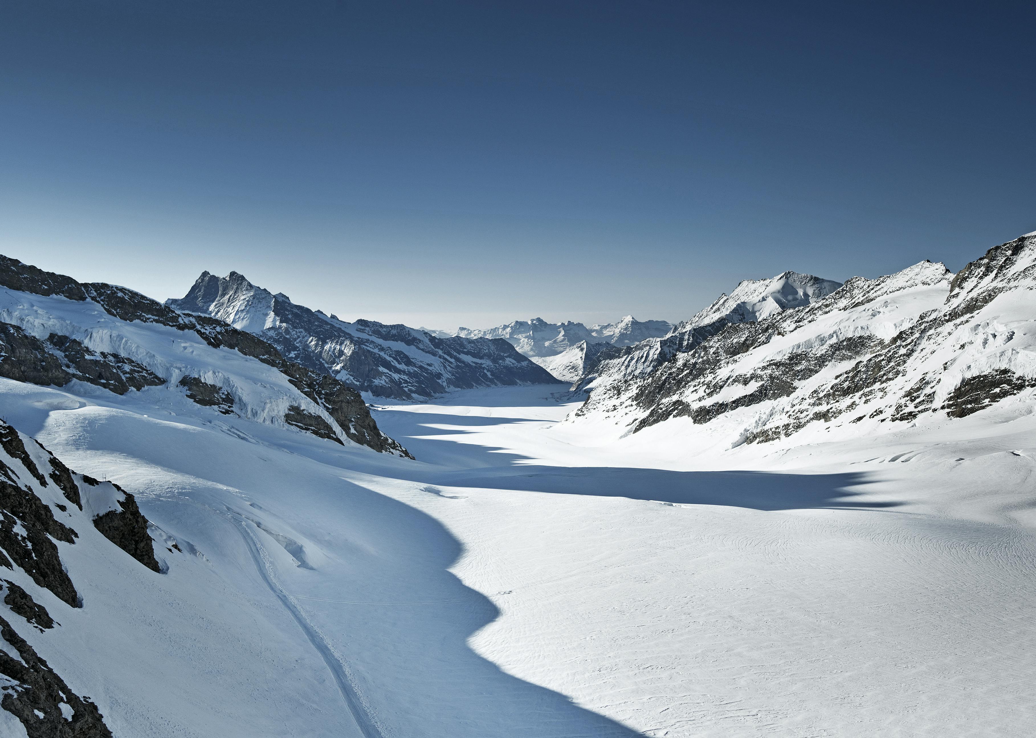 Zasněžené hory a údolí pod jasnou modrou oblohou s nedotčeným nedotčeným sněhem rozprostírajícím se po celé krajině.