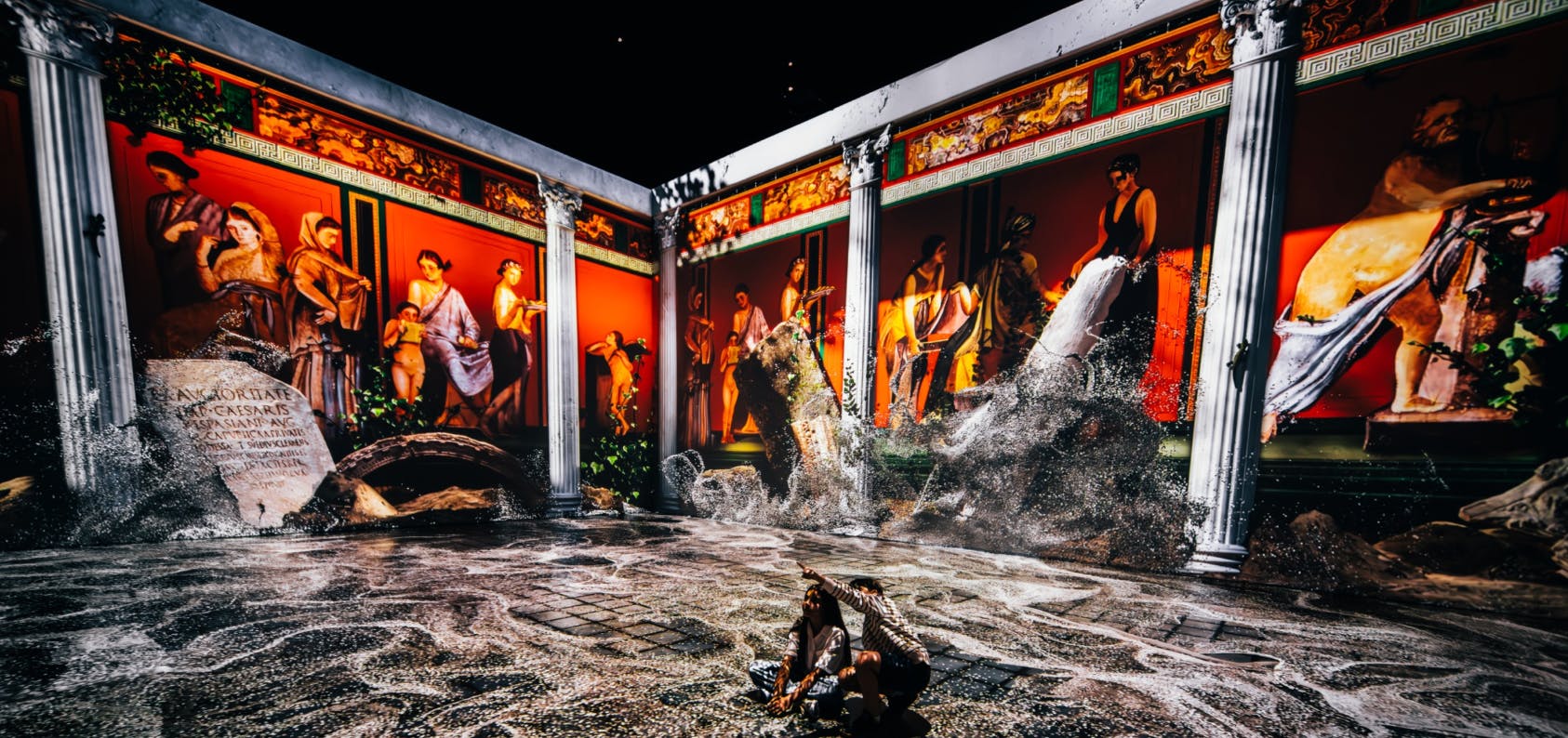 Una colorida instalación artística inmersiva que representa antiguos frescos romanos con efectos de agua y visitantes interactuando.