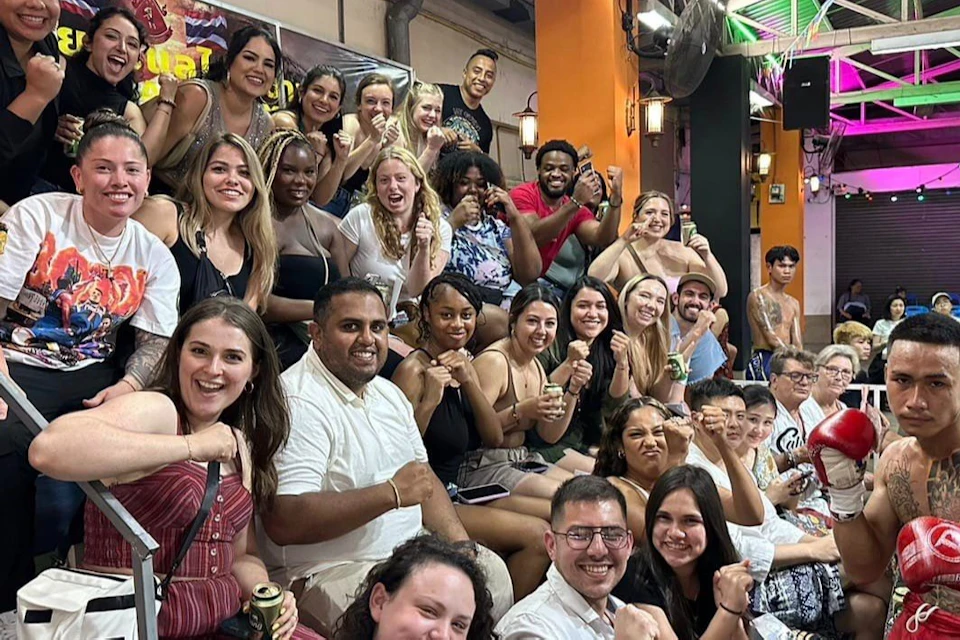 A group of people seated together indoors, some of them posing with fists raised in a lively and cheerful atmosphere.