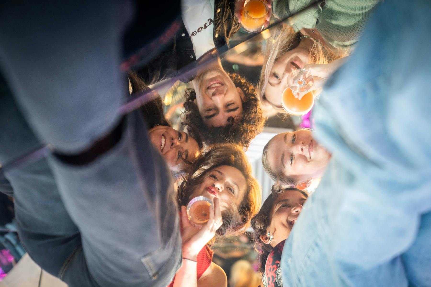 笑顔でグラスを上げながら飲み物を飲んでいる6人の友人のグループ。下から見ています。