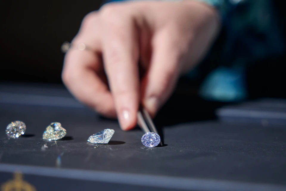 A hand holding tweezers is picking up a gemstone from a group of three on a table.