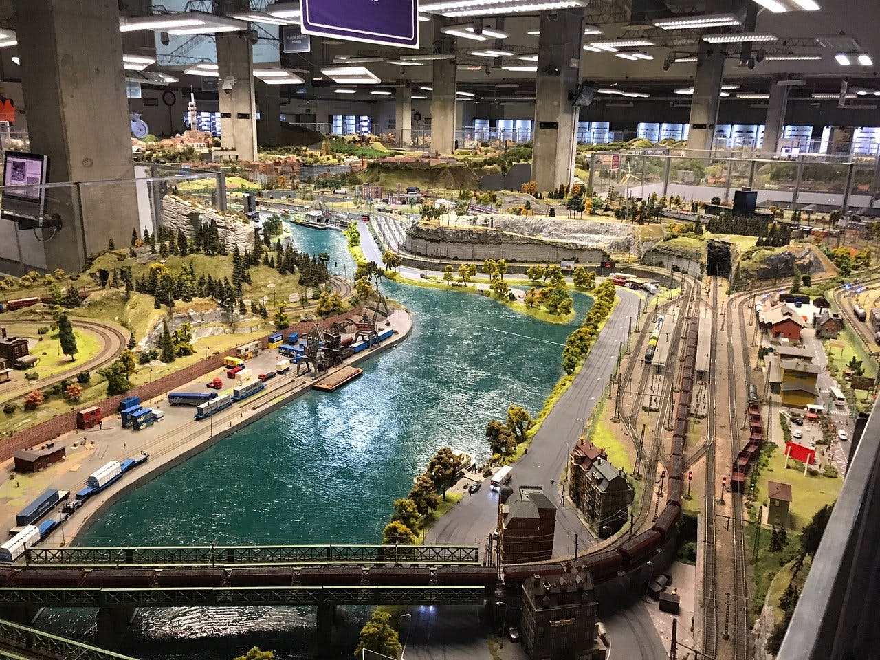 详细的铁路模型布局，包括火车、轨道、道路、建筑物、树木和流经场景的河流。