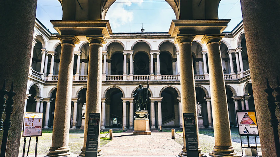 An arched courtyard with large columns, a central statue, and a two-story building with multiple archways in the background.