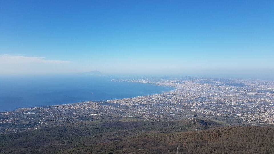 Aerial view of a coastal city with sprawling urban areas next to a large body of water, under a clear blue sky.